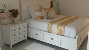 Une chambre à coucher avec un lit blanc, une table de chevet, une commode et un miroir.