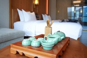 A hotel room with a neatly made bed, a wooden bedside table with a tray of green teapots and cups, and a wooden headboard. - Xindalu International Hotel (Yuanjiang)
