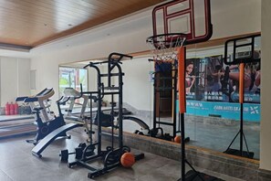 A gym with exercise equipment, a basketball hoop, and a mirror reflecting the gym area. - Xindalu International Hotel (Yuanjiang)