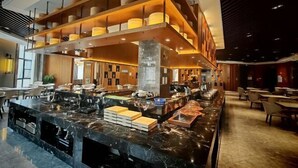 A modern hotel lobby with a marble reception desk, wooden shelving with decorative items, and a seating area with tables and chairs. - Xindalu International Hotel (Yuanjiang)