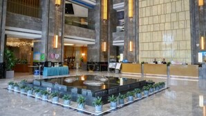 A spacious lobby with a central water feature, multiple reception desks, and a modern design with vertical lighting elements. - Xindalu International Hotel (Yuanjiang)