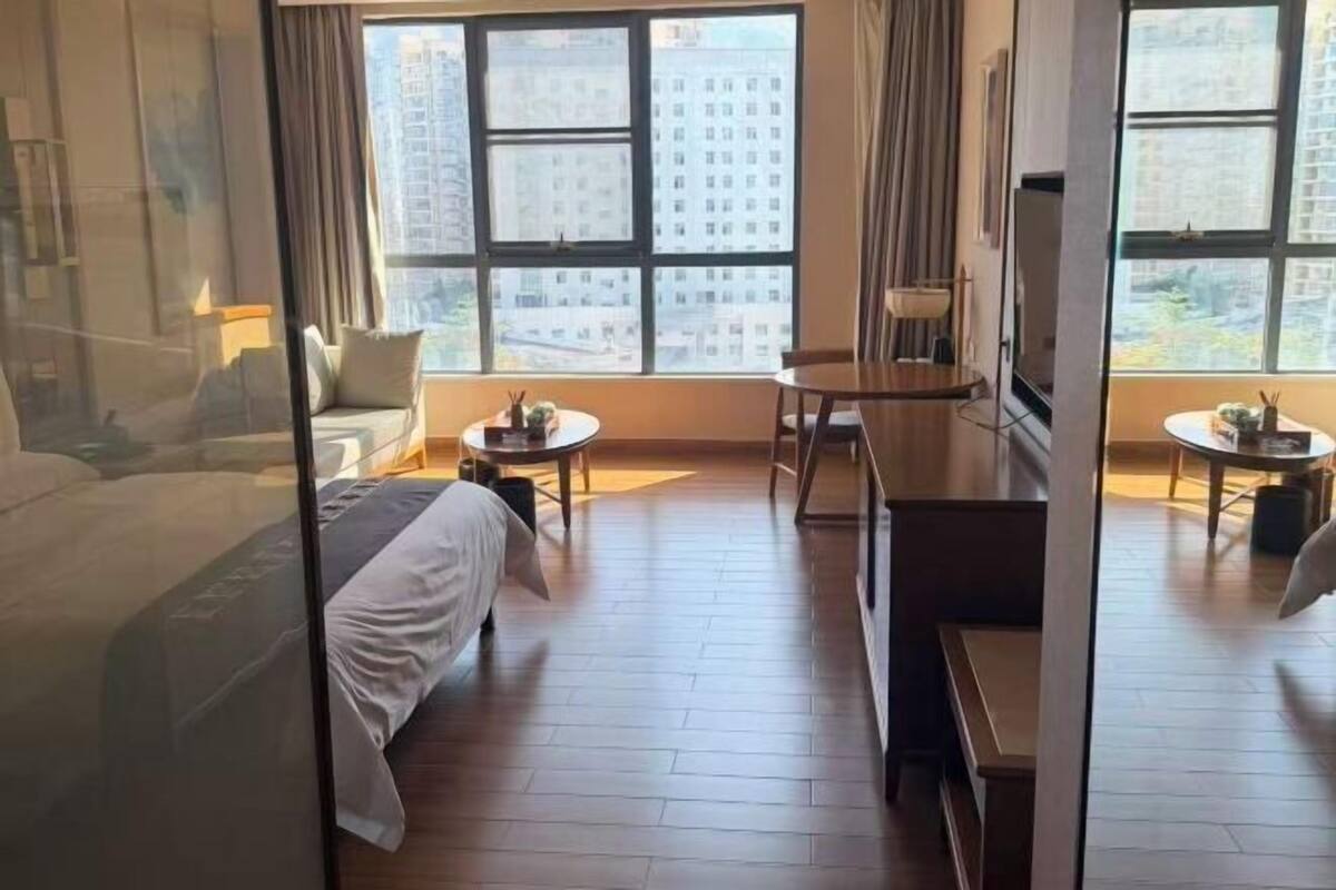Habitación de hotel con cama, escritorio, silla, mesita y ventanas amplias con vistas a la ciudad.
