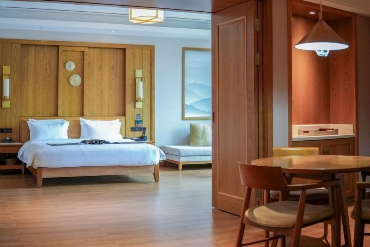Habitación de hotel con cama, mesita de noche, lámpara y zona de comedor con sillas.