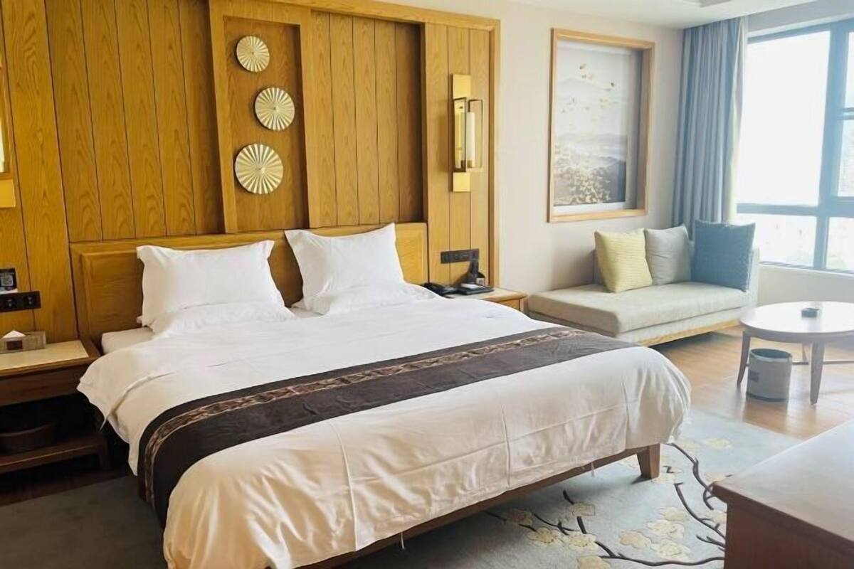 Una habitación de hotel con una cama grande, un sofá, una mesita y una ventana con cortinas.