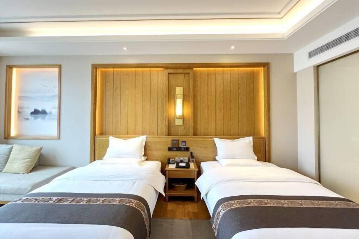 Habitación de hotel con dos camas, cabecera de madera, mesita de noche con lámpara y un cuadro enmarcado en la pared.
