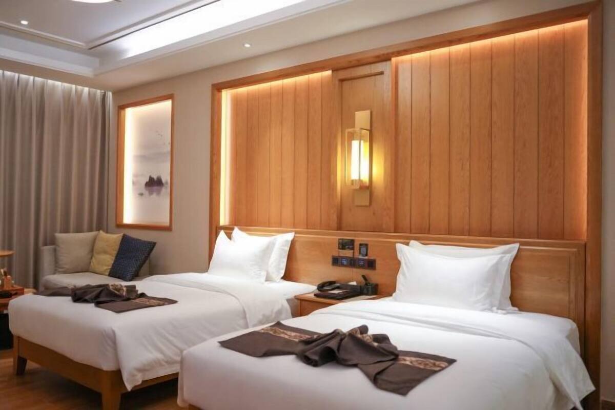 Habitación de hotel con dos camas, cabecero de madera, mesita de noche y ventana con cortinas.