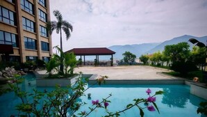 A swimming pool with a view of mountains, a covered pavilion, and a tall building. - Xindalu International Hotel (Yuanjiang)
