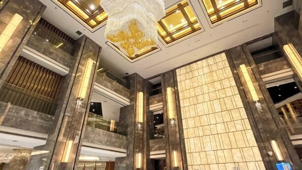 A modern interior with a high ceiling, reflective surfaces, and warm lighting. - Xindalu International Hotel (Yuanjiang)