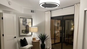 Ein Hotelzimmer mit Bett, Stuhl, Lampe, Topfpflanze, Gemälde und einer Glasschiebetür, die auf einen Balkon führt.