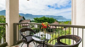 Ein Balkon mit einem Glastisch, zwei Korbstühlen und einer Blumenvase.