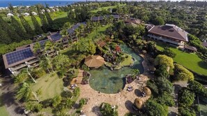 Eine Vogelperspektive zeigt ein Resort mit mehreren Gebäuden, einem Schwimmbecken und umliegender Bepflanzung.