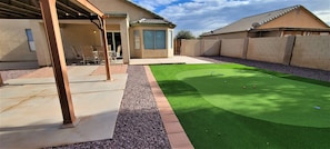 A backyard with artificial turf, a patio area, and a covered seating space.