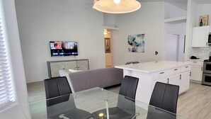 Une cuisine moderne avec des meubles blancs, un îlot central et un coin repas comprenant une table en verre et des chaises noires.