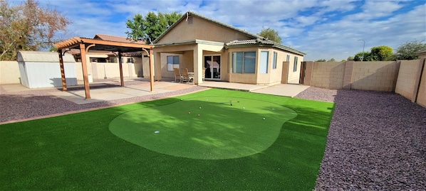 A backyard with artificial turf, a pergola, and a house with a garage.