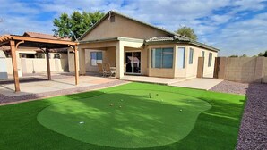 Une maison dotée d’un jardin avec une pelouse artificielle, un espace vert aménagé en putting green et une petite piscine.