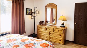 A bedroom with a bed, a wooden dresser, a mirror, a lamp, and a door.