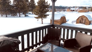 Eine Holzterrasse mit Korbstühlen und einem Tisch, mit Blick auf eine verschneite Landschaft mit Holzhütten.