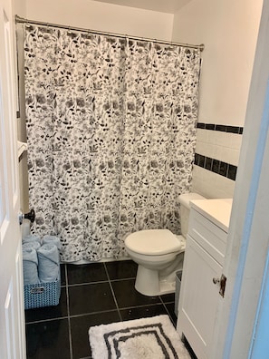 A bathroom with a floral shower curtain, a white toilet, and a blue patterned rug.