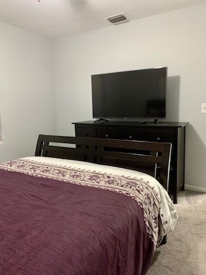 A bedroom with a bed, a dresser, and a television on top of the dresser.