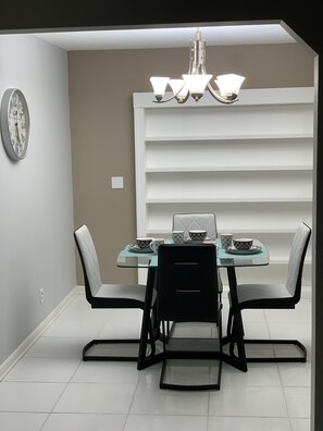 A dining area with a table set for four, chairs, a chandelier, and a wall-mounted shelf unit.