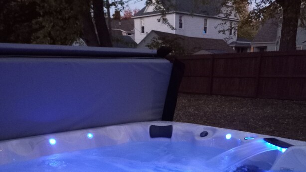 Un jacuzzi con luces LED azules, rodeado por una valla de madera y árboles.