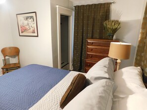 A bedroom with a bed, a dresser, a chair, a lamp, and a painting on the wall. - Fit For a Crew With A Hot Tub Too-5 bedroom (Pekin)