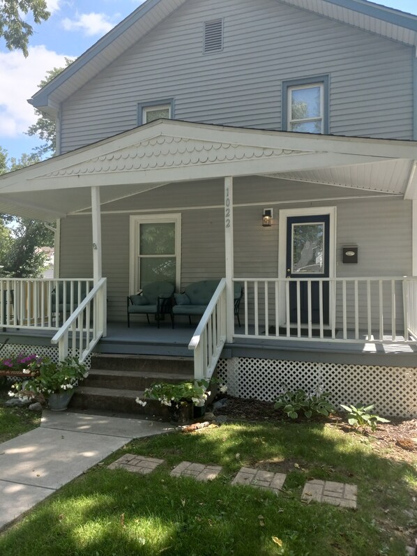 A two-story house with a covered porch, a front door, and a small front yard with potted plants. - Fit For a Crew With A Hot Tub Too-5 bedroom (Pekin)
