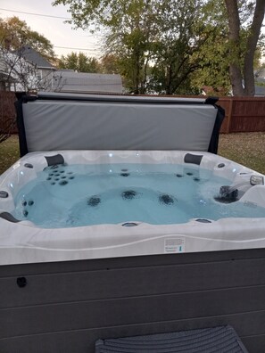 A hot tub with a cover, bubbles, and a label indicating a brand. - Fit For a Crew With A Hot Tub Too-5 bedroom (Pekin)