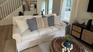 A living room with a white sofa, a wicker coffee table, and a staircase with blue accents.