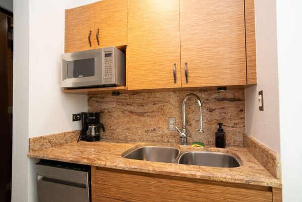 A kitchen with wooden cabinets, a stainless steel sink, a microwave, and a coffee maker. - Pelican Reef 703 Beachfront Penthouse with Ocean and Sunset Views (Stella)