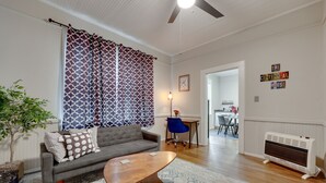 A living room with a grey sofa, a wooden coffee table, patterned curtains, a blue chair, and a radiator.