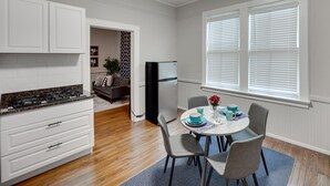A kitchen with white cabinets, a stove, and a refrigerator. There is a dining area with a table, chairs, and blue tableware.