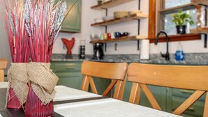 A kitchen with wooden chairs, a table with a vase of wheat stalks, and shelves with kitchen items. - Scenic Deep Creek Getaway Cabin-RICK'S RETREAT (Oakland)