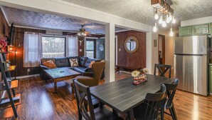 A cozy living room with a dark wooden dining table, a leather sofa, and a chandelier. - Scenic Deep Creek Getaway Cabin-RICK'S RETREAT (Oakland)