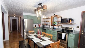 A modern kitchen with green cabinets, stainless steel appliances, and a wooden dining table with papers. - Scenic Deep Creek Getaway Cabin-RICK'S RETREAT (Oakland)