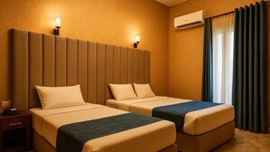 Habitación de hotel con dos camas, una mesita de noche, un equipo de aire acondicionado y una ventana con cortinas.