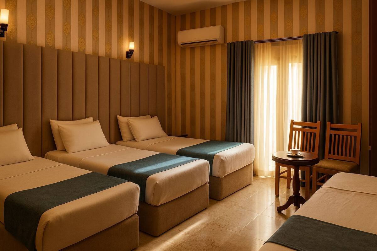 A hotel room with three beds, a small table with chairs, and an air conditioning unit on the wall.