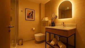 Un baño moderno con cabina de ducha de vidrio, inodoro, lavamanos con espejo y una obra de arte enmarcada en la pared.