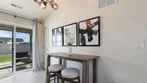 A modern kitchen with a wooden table and two stools, a large window with a view of the backyard, and three framed artworks on the wall. - Modern Caldwell Home | Near Freeway & Shopping | Sleeps 10 (Caldwell)