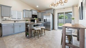 A modern kitchen with grey cabinets, stainless steel appliances, and a central island with stools. - Modern Caldwell Home | Near Freeway & Shopping | Sleeps 10 (Caldwell)