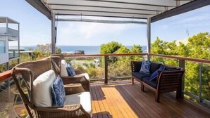 A covered outdoor deck with wicker furniture and a view of the ocean.