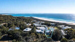 An aerial view of a coastal residential area with houses, a beach, and a clear sky.