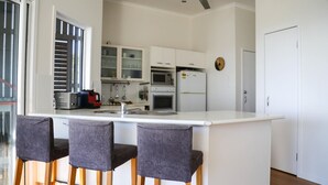 A modern kitchen with a central island, bar stools, white cabinets, a microwave, an oven, and a refrigerator.