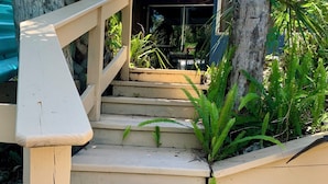 Un escalier en bois de couleur beige mène à un espace extérieur abrité, doté d’une rambarde en bois.