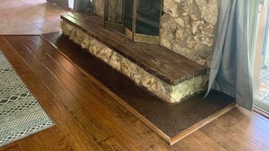 Une cheminée en pierre surmontée d’un téléviseur à écran plat, un plancher en bois et, au fond, un coin cuisine.