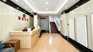 Zona de recepción de un hotel, con mostrador, una escalera y un reloj en la pared.