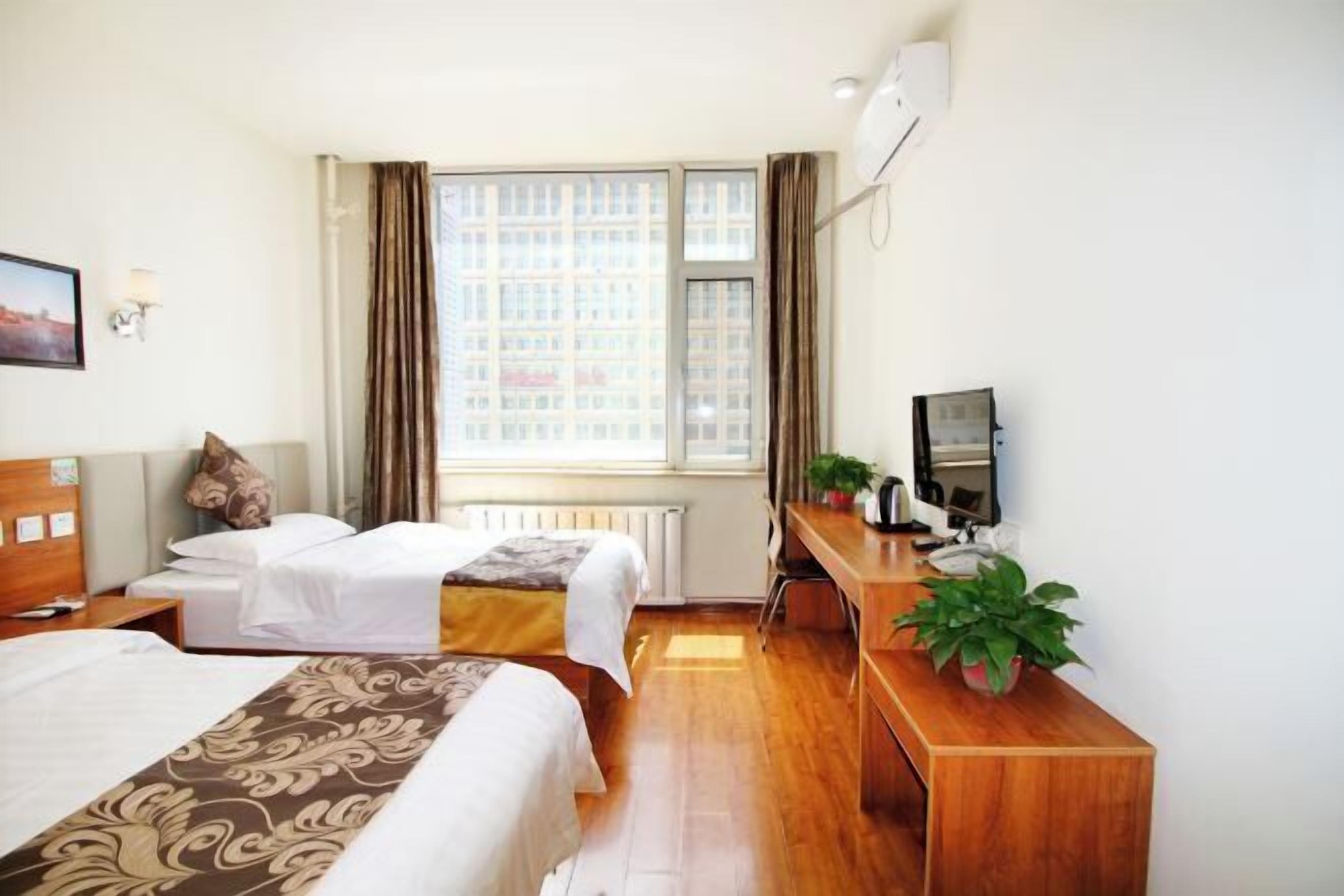 A hotel room with two beds, a desk with a computer, a TV, and a window with curtains.