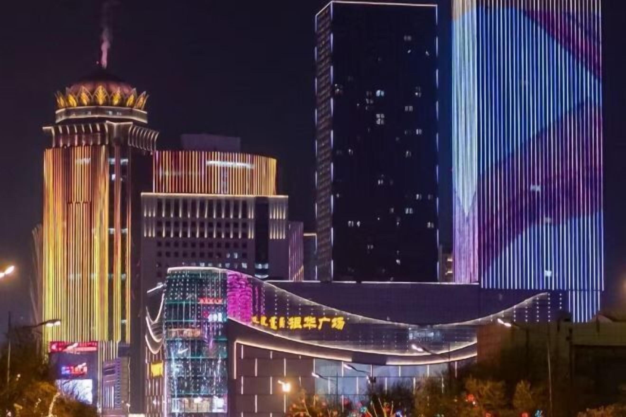 A cityscape at night with illuminated buildings, including a prominent tower and a curved structure with signage.