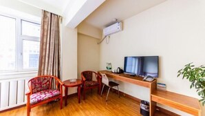 Una habitación con un escritorio de madera, televisor, radiador y ventana con cortinas.