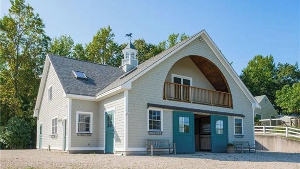 A two-story building with a gabled roof, a balcony on the upper floor, and a small tower with a weathervane. - Farm Stay with Horses & Pool with Mountaintop Views (Bloomfield)